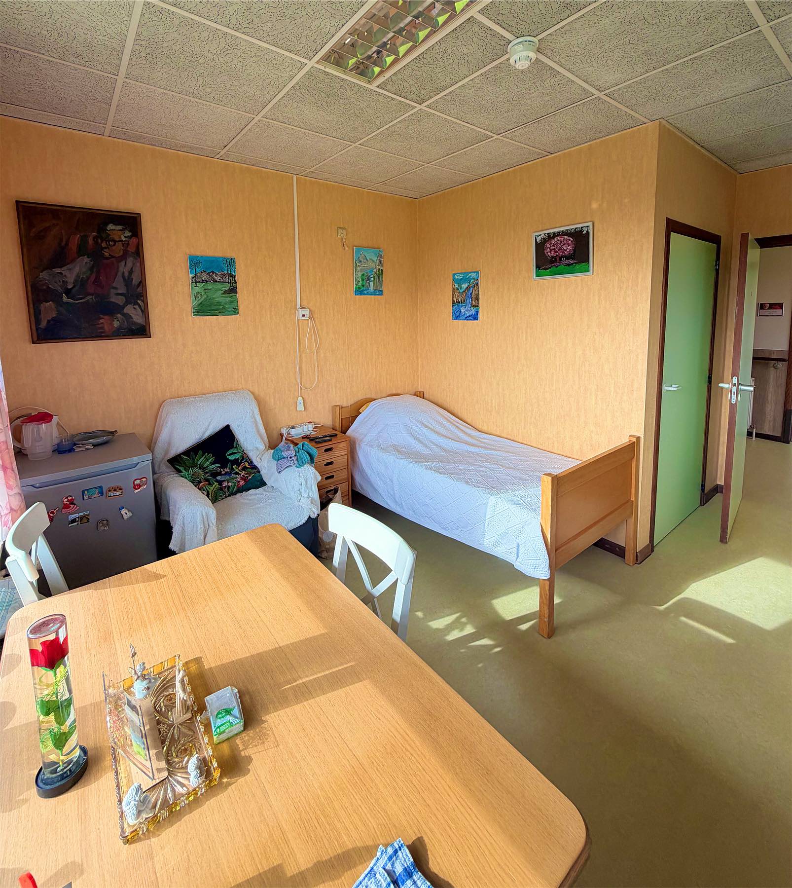 Chambre individuelle avec lit, fauteuil et tableaux aux murs