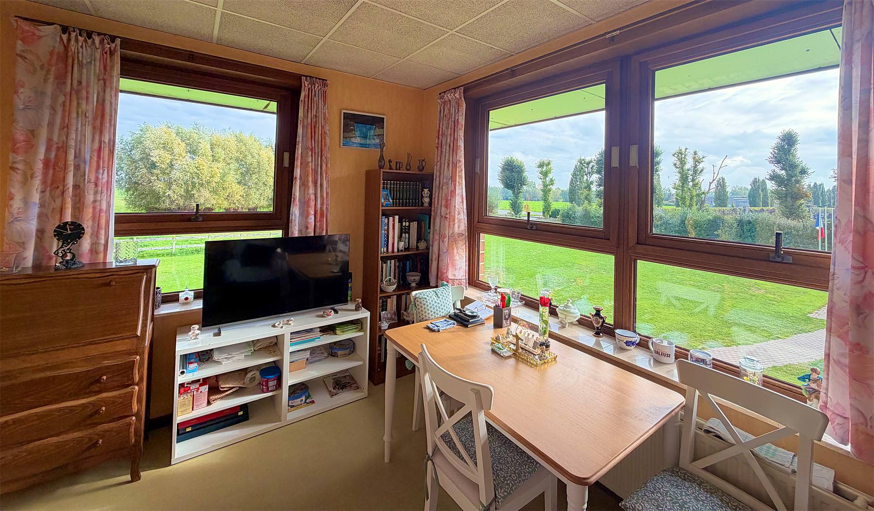 Chambre individuelle lumineuse avec table, télévision et vue sur les champs