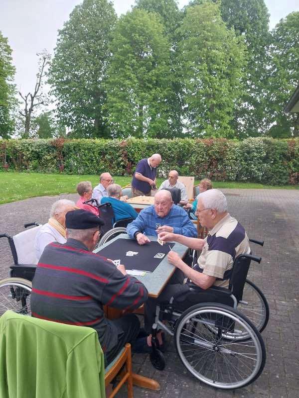 Des résidents jouent aux cartes dehors, sous les arbres