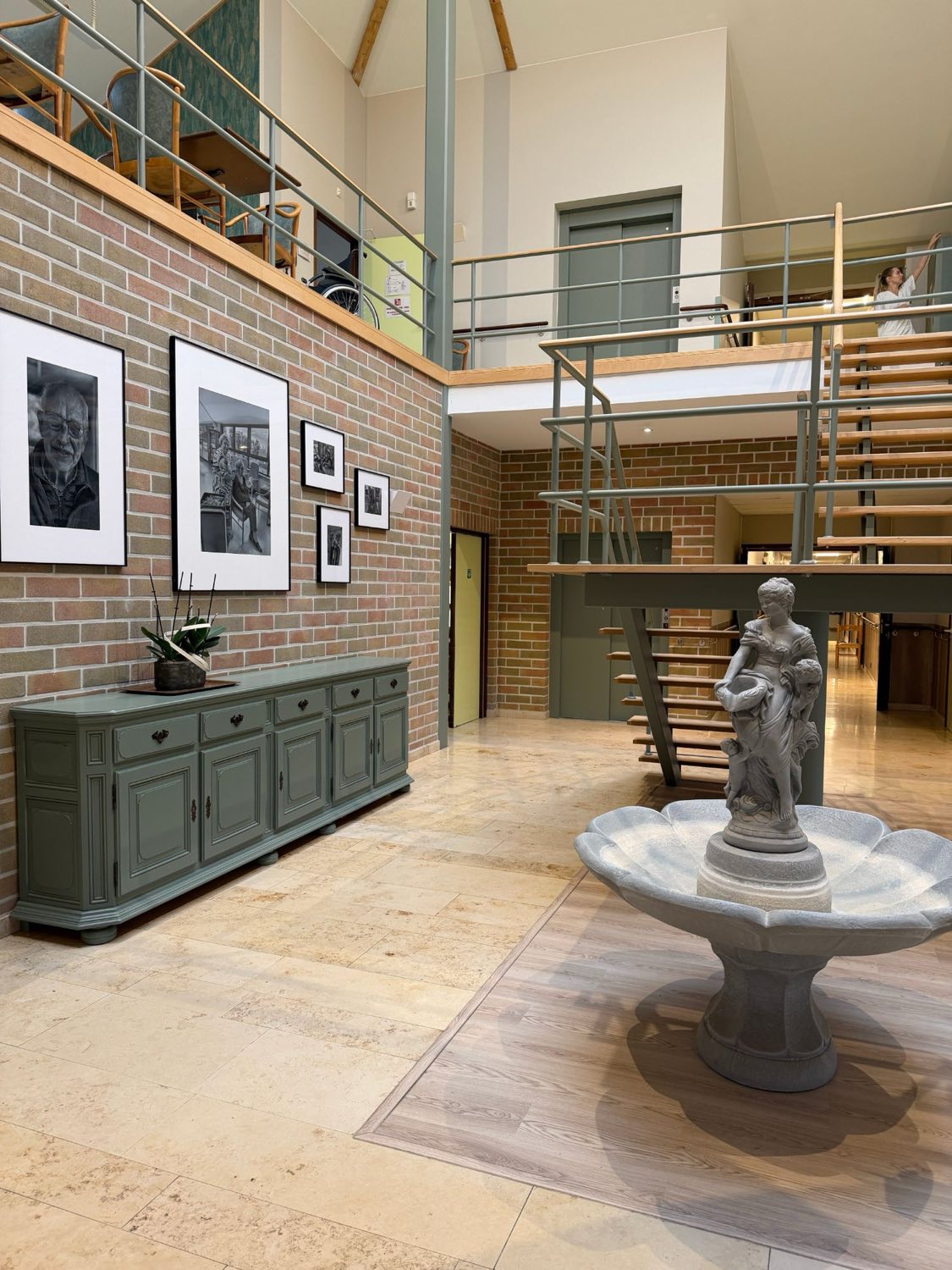Le hall d'entrée avec sa fontaine, son buffet vert et ses portraits en noir et blanc, sous la mezzanine