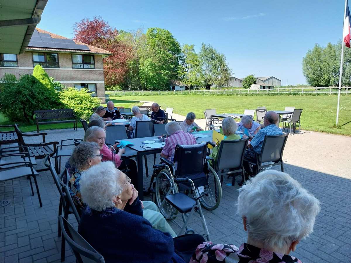 Des résidents réunis sur la terrasse ensoleillée, face à la grande pelouse et aux arbres du jardin