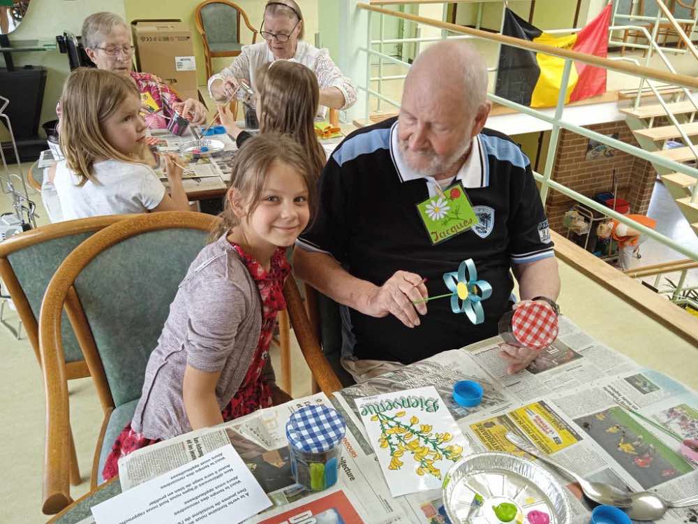 Une écolière et un résident, souriants, peignent ensemble des pots lors d'une rencontre avec l'école